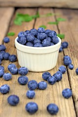 Healthy food,agriculture,harvest and fruit concept: close-up ripe blueberries sprinkled next to a white bowl on a wooden background.