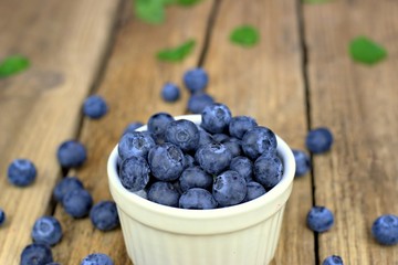 Healthy food,agriculture,harvest and fruit concept: close-up ripe blueberries sprinkled next to a white bowl on a wooden background.