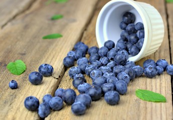 Healthy food,agriculture,harvest and fruit concept: close-up ripe blueberries sprinkled next to a white bowl on a wooden background.