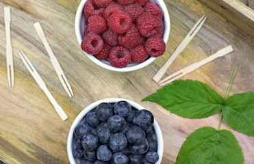 Healthy food,agriculture,harvest and fruit concept: fresh ripe blueberries and raspberries in two bowls on a wooden tray.