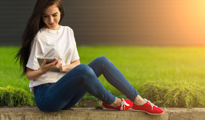 young brunette womanwith tablet serfing in internet on grass