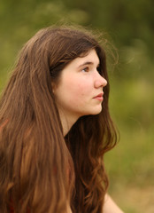 teenager girl with long thick brown hair outdoor portrait on green summer field background