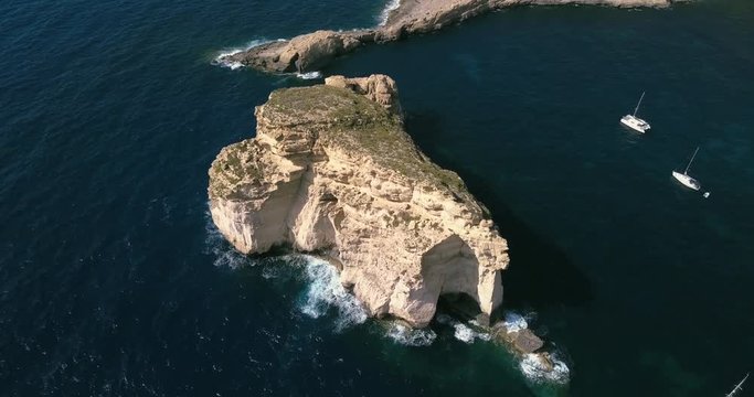 Aerial view of small rocky island in the blue sea with sailing boats in the bay wit cliffs. Gozo, Malta