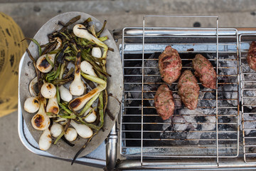 Onions and lamb kofta cooking on a charcoal grill