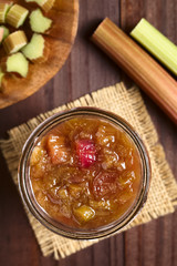 Homemade rhubarb jam in jar with raw rhubarb on the side, photographed overhead (Selective Focus, Focus on the jam)