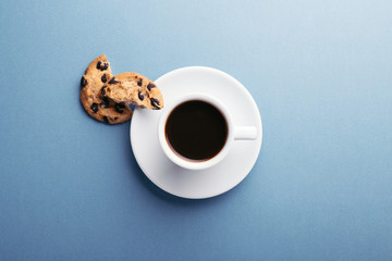 A cup of coffee and american cookies with chocolate chips on blue grey background. Top view.