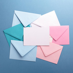 Group of colorful envelopes on grey table with empty card. Correspondence concept. Mockup.