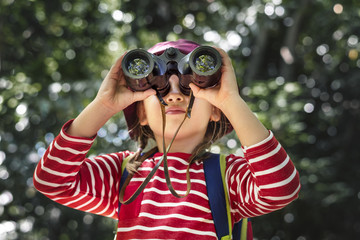 Little girl using binoculars in the forest