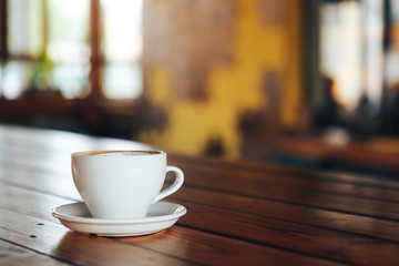 Hot coffee in white cup on wooden table. White cup of coffee on a wooden table in a cafe. Good morning with a ceramic white cup of coffee in a cafe 