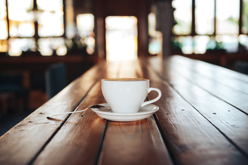 Hot coffee in white cup on wooden table. White cup of coffee on a wooden table in a cafe. Good morning with a ceramic white cup of coffee in a cafe 