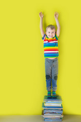 A joyful smiling child is standing on a stacked of children's books. Green background.