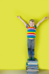 A joyful smiling child is standing on a stacked of children's books. Green background.