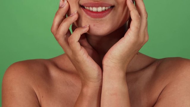 Cropped studio shot of a happy beautiful woman with sexy plump lips and healthy white teeth smiling joyfully, cupping her face with her hands. Stunning female on green chromakey.