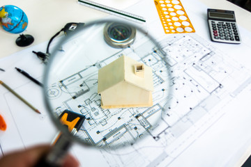Magnifying glass on a house model on architecture plan background. Engineering table topview.