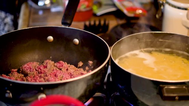 Close up on spaghetti ingredients cooking - meat browning and noodles boiling