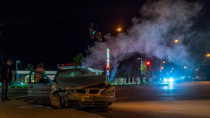 Close up of a car crushed in an accident, smoke and flares in the background.