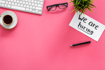 Search for worker, employee concept. We are hiring lettering on work desk on pink background top view copy space