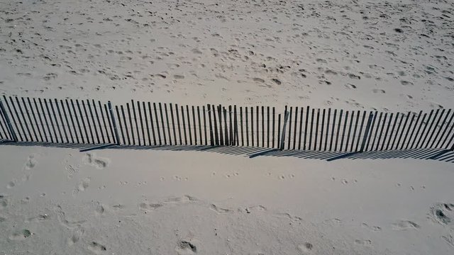 Low Aerial: Footsteps recorded in the sand near a wooden fence on the beach