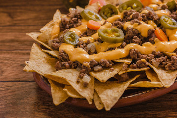 nacho chips corn garnished with ground beef, melted cheese, jalapeños peppers in plate on wooden...