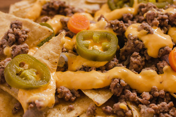 nacho chips corn garnished with ground beef, melted cheese, jalapeño peppers in plate on wooden table mexican spicy food in mexico
