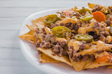 nacho chips corn garnished with ground beef, melted cheese, jalapeño peppers in plate on wooden table mexican spicy food in mexico