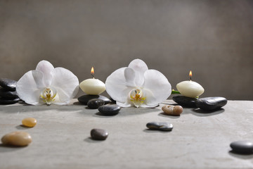 Fototapeta na wymiar candle with pile of black stones and white orchid on gray background