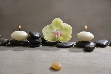 Obraz na płótnie Canvas candle with pile of black stones and yellow orchid, herbal ball.towel on gray background