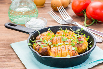Baked young potatoes in spices and oil with arugula in a iron pan and sour cream on a wooden table