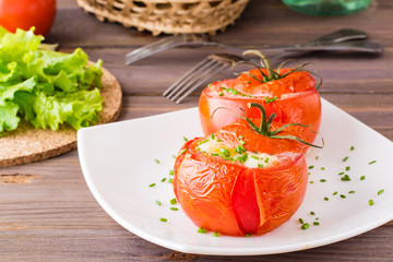 Fresh tomatoes baked with cheese and egg sprinkled with green onions on a plate on a wooden table