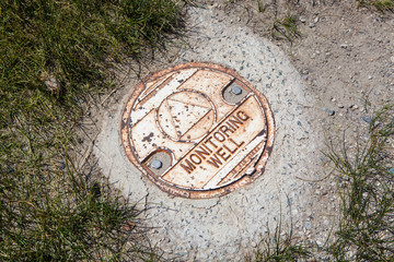 Old Decayed Monmitoring Well Lid Set in Concrete, Surrounded by Soil and Grass