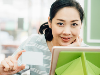 Happy woman is using a white mockup credit card for online shopping on tablet.