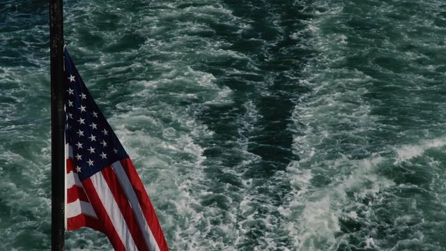 An American Flag hovers over the wake of a boat. (POV from Rear of boat)