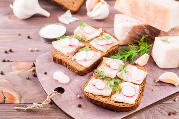 Sandwiches from rye bread, salted bacon, radish and dill on a cutting board on a wooden table