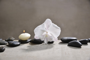 Obraz na płótnie Canvas candle with pile of black stones and white orchid, on gray background
