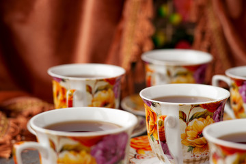 Tea set in brown and red tones. Six cups of tea in a tea set against a background of brown velvet curtains.