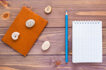 Clean open notepad for writing, pencil, passport and seashell on a wooden background. Top view. Vacation concept.