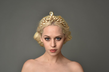 portrait of blonde woman wearing golden crown, grey studio background.