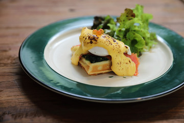 Breakfast food egg benedict , poached egg with yellow sauce with waffle and smoked salmon on wood background