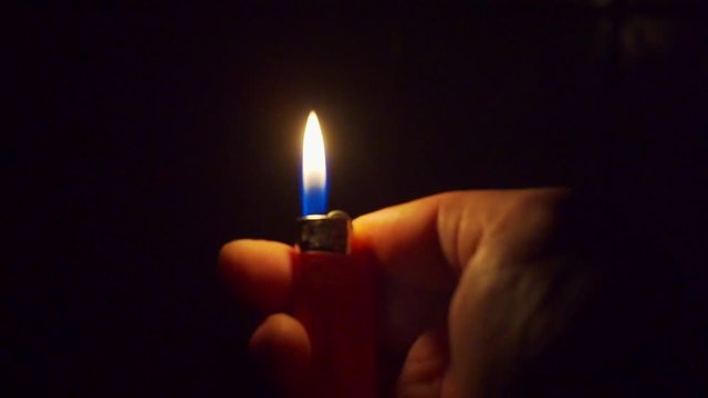 hand holds a burning lighter in the dark
