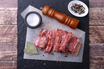 Raw fresh meat, uncooked lamb or beef ribs with pepper, garlic, salt, bay leaves and spices on dark stone background, Ready for cooking. copy space.
