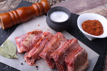 Raw fresh meat, uncooked lamb or beef ribs with pepper, garlic, salt, bay leaves and spices on dark stone background, Ready for cooking. copy space.