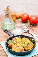 Baked young potatoes in spices and oil with arugula in a iron pan and sour cream on a wooden table