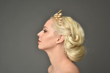 portrait of blonde woman wearing golden crown, grey studio background.