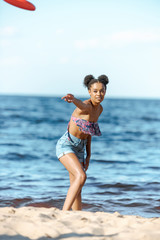 african american woman throwing flying disc on sandy beach