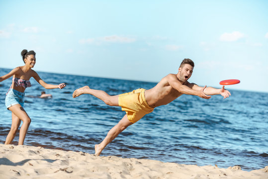 young multicultural couple playing with flying disc on beach on summer day - Powered by Adobe
