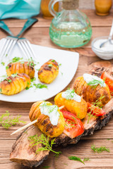 Baked potatoes on skewers with sour cream, tomato  and herbs on a bark of tree