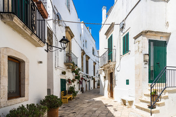 Fototapeta na wymiar A street in Locorotondo with typical whitewashed houses and hanging flowers, Apulia, Italy