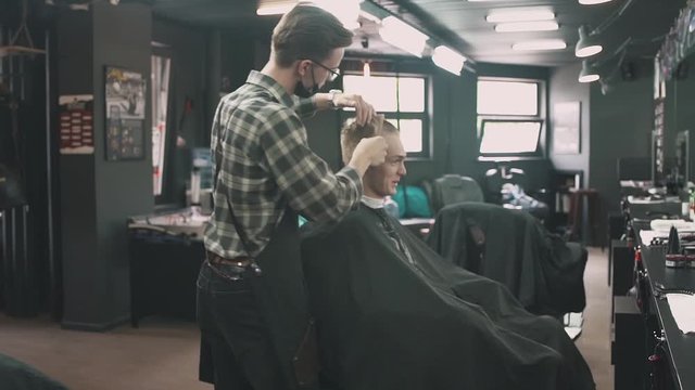 Barbershop, hairdresser combs hair to a man.
