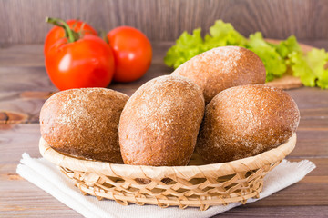 Fresh rye buns in a basket, salad and tomato on a wooden table