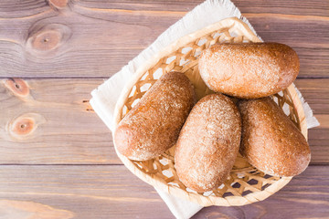 Fresh rye buns in a basket on a wooden table. Top view. Copy space